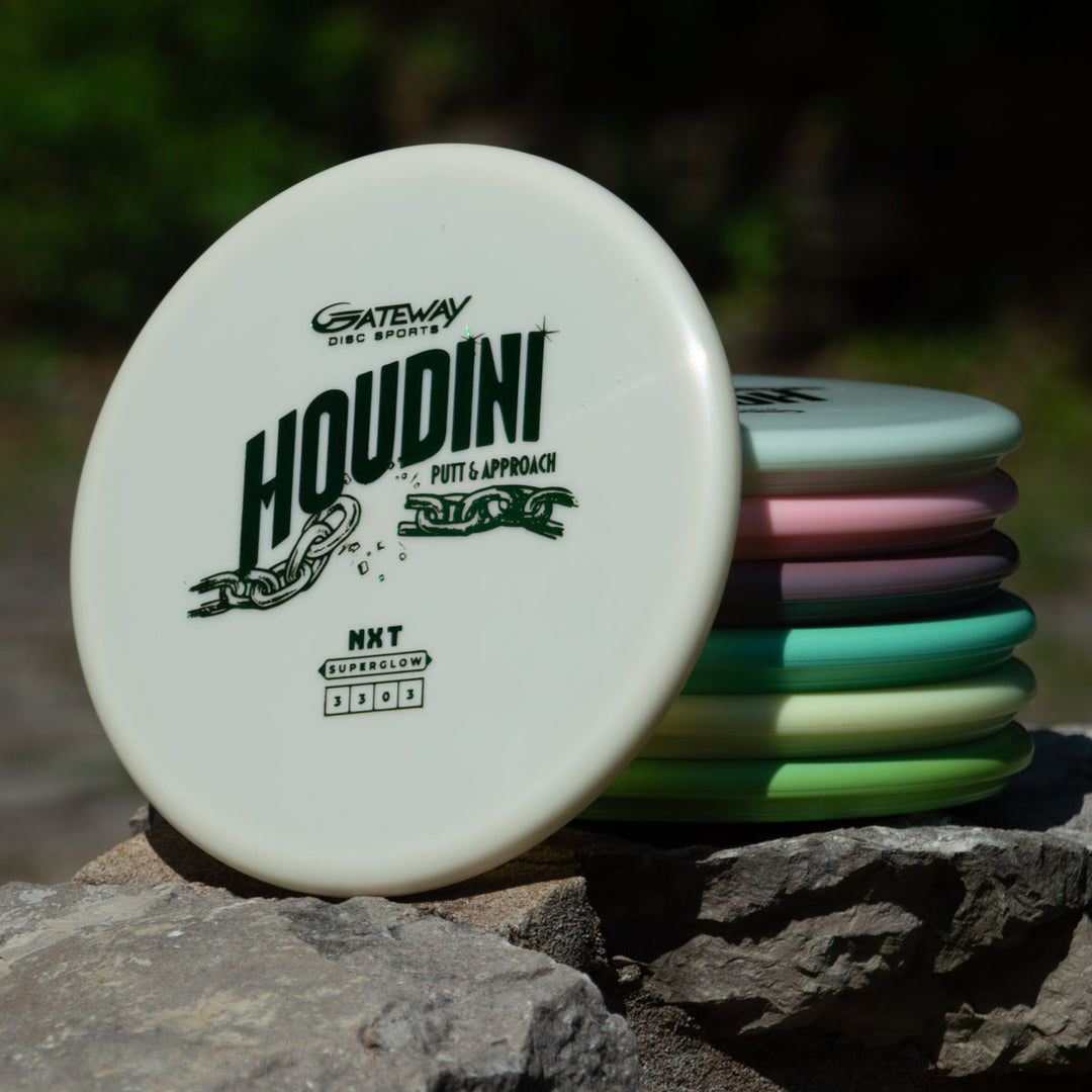 A stack of Houdini - NXT Superglow putt and approach discs sits on a rock, with one white disc showing the logo in front€”ideal for power-grip backhands.
