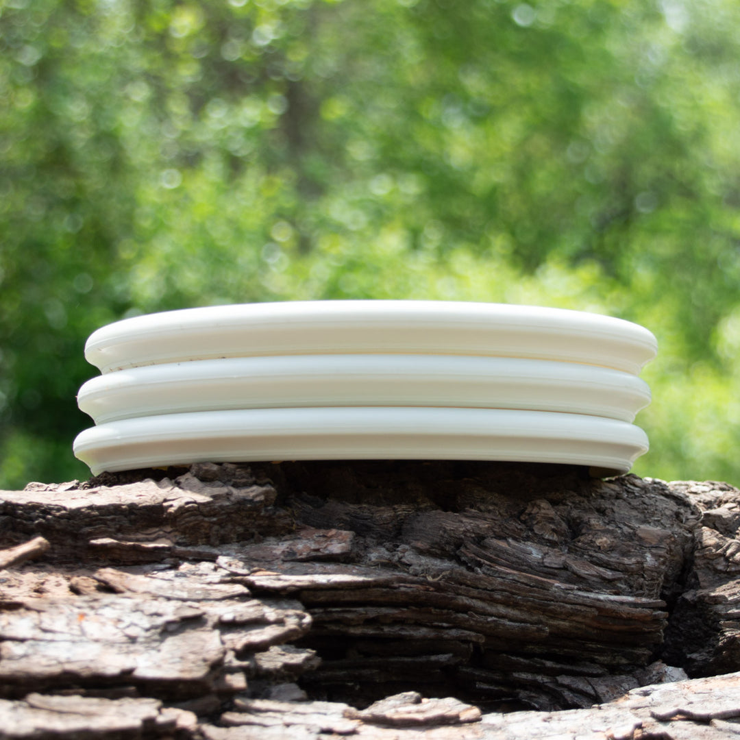 Four Houdini - SureGrip™Superglow plates, featuring a deep rim design inspired by putt and approach discs, are stacked together on rough wood with a blurred green backdrop.
