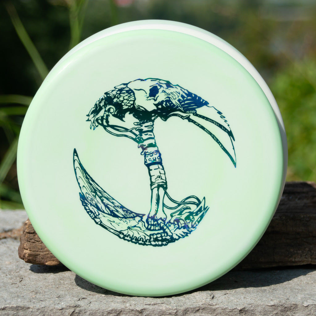 A pale green Brett Stetson Houdini Superglow disc with art by Kevin Hart, featuring a detailed dark blue double-bladed axe and intricate designs, ideal for putt and approach in disc golf.