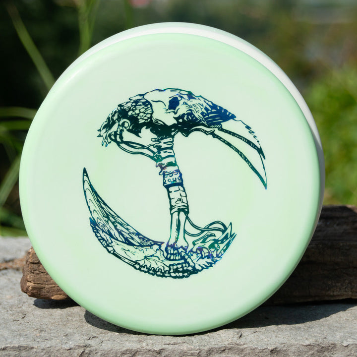 A pale green Brett Stetson Houdini Superglow disc with art by Kevin Hart, featuring a detailed dark blue double-bladed axe and intricate designs, ideal for putt and approach in disc golf.