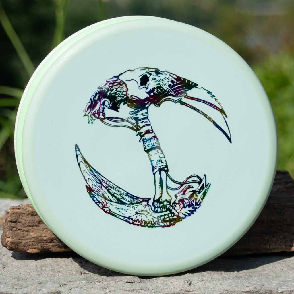 The Brett Stetson Houdini Superglow disc, featuring Kevin Hart's vibrant skeletal bird head and talon crescent design, stands upright on an outdoor stone surface€”ideal for your next disc golf tour.