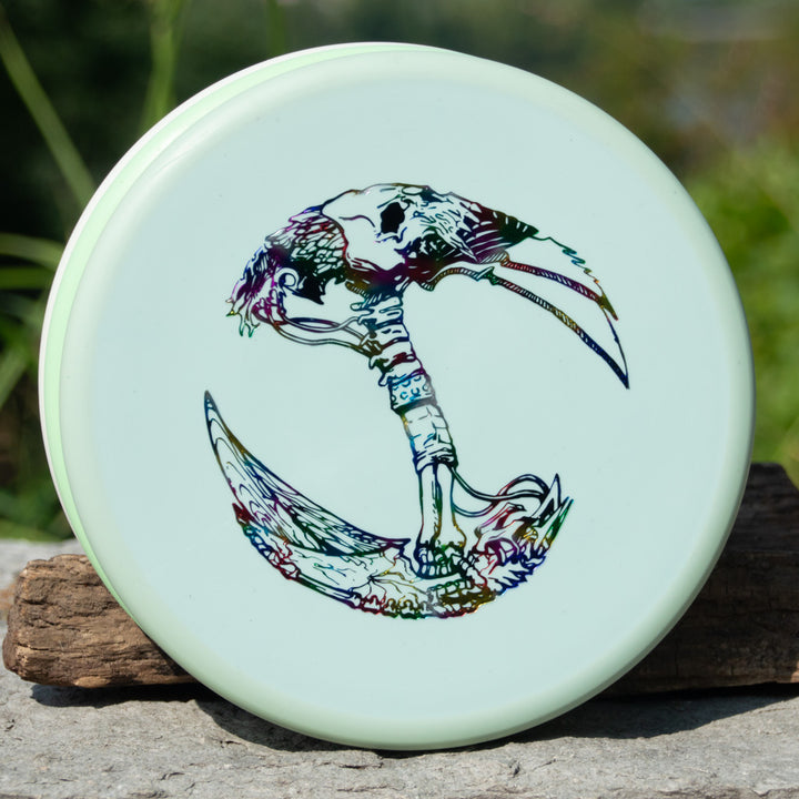 The Brett Stetson Houdini Superglow disc, featuring Kevin Hart's vibrant skeletal bird head and talon crescent design, stands upright on an outdoor stone surface€”ideal for your next disc golf tour.