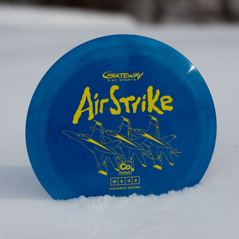 A blue Airstrike - Cobalt disc golf driver by Gateway Disc Sports, featuring yellow "Air Strike" text and three jet illustrations, stands upright on snow.