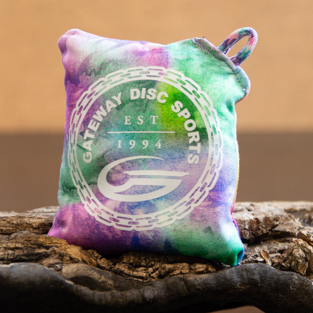 The Gateway Disc Sports x Jaybirdz Dry Bag — Grip-Enhancing Chalk Bag features a colorful tie-dye design with "Gateway Disc Sports EST 1994" and a chain logo, displayed on a wooden surface.