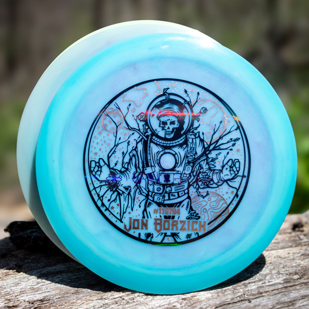 Gateway Disc Sports' Jon Borzick's Ether - Color Superglow is a turquoise distance driver featuring a skeleton astronaut graphic, Jon Borzick's name, and #110194, all printed on durable NXT material.