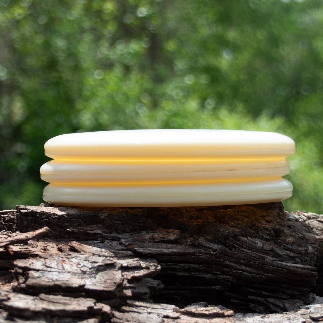Three Magic - Diamond putter discs are stacked on rough bark with blurred green foliage in the background—perfect for anyone seeking a reliable beginner or straight-flying disc for their game.