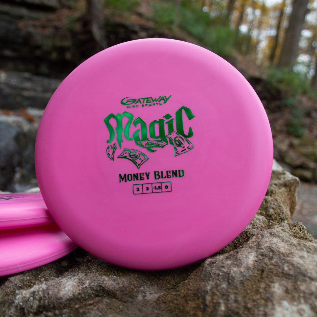 A pink Magic - Money beginner-friendly putter from Gateway Disc Sports sits on a rock outdoors, featuring "Money Blend" text.