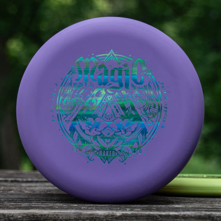 A purple Magic - Suregrip NAKED disc golf putter with intricate blue-green designs rests on a wooden surface outdoors, ready for smooth, straight flights and exceptional glide.