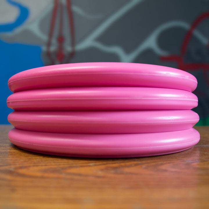 Four stacked Voodoo - Money discs rest on a wooden surface, standing out against a blurred, multicolored background.