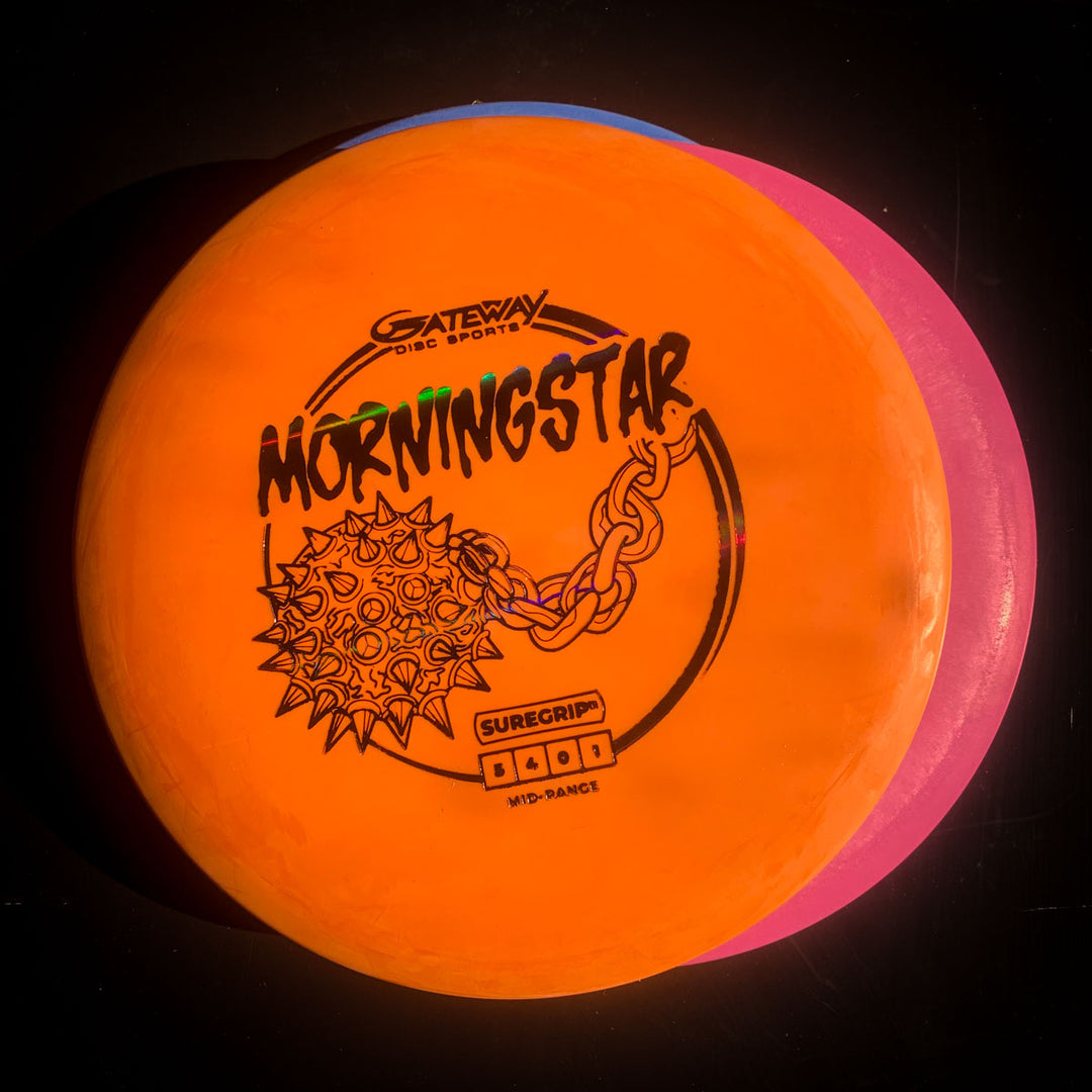 An orange Morningstar - Suregrip disc golf mid-range, known for its neutral flight, is stacked on a pink disc against a black background.