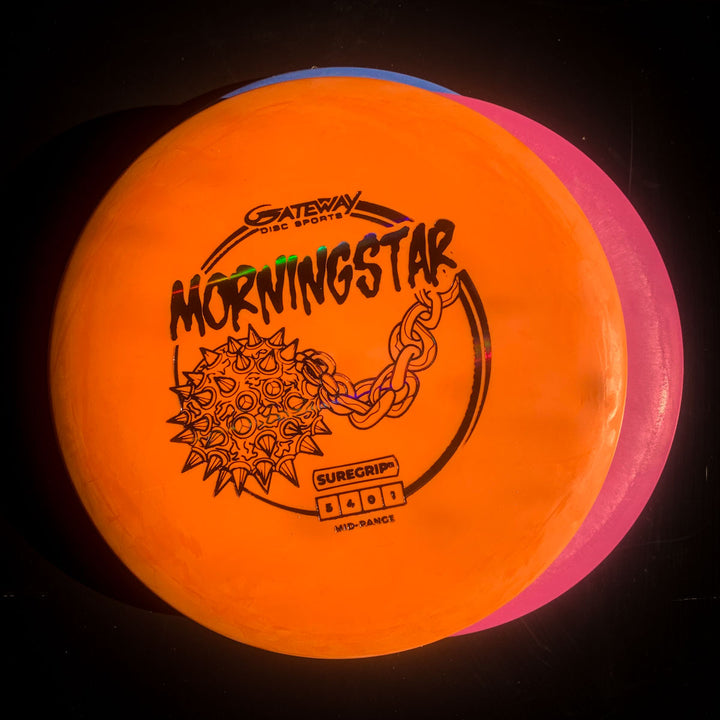 An orange Morningstar - Suregrip disc golf mid-range, known for its neutral flight, is stacked on a pink disc against a black background.