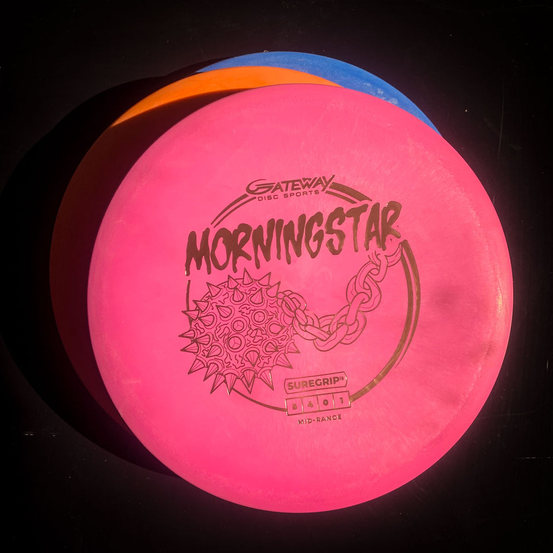 A pink Morningstar - Suregrip neutral flying mid-range disc is stacked on blue and orange discs, all against a black background.