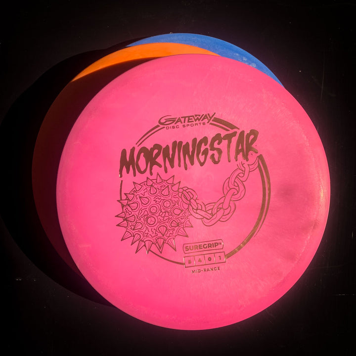 A pink Morningstar - Suregrip neutral flying mid-range disc is stacked on blue and orange discs, all against a black background.