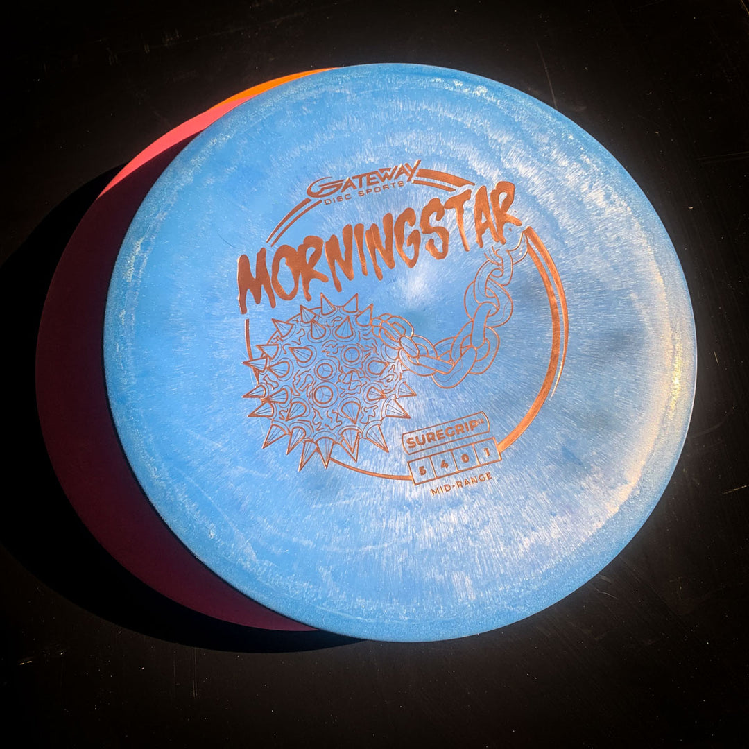 A blue Gateway Morningstar - Suregrip disc golf disc, featuring a morningstar weapon graphic, rests on a dark surface. This neutral-flying mid-range is ideal for versatile throws.