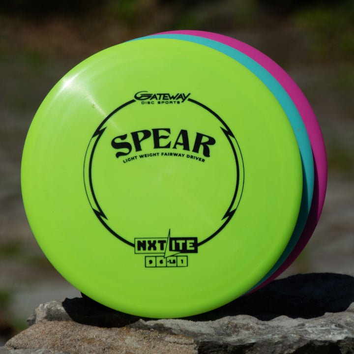 Three disc golf discs are stacked on a rock outdoors, with the front one being the Spear - NXT LITE by Gateway Disc Sports—ideal for accurate placement and control driver performance.