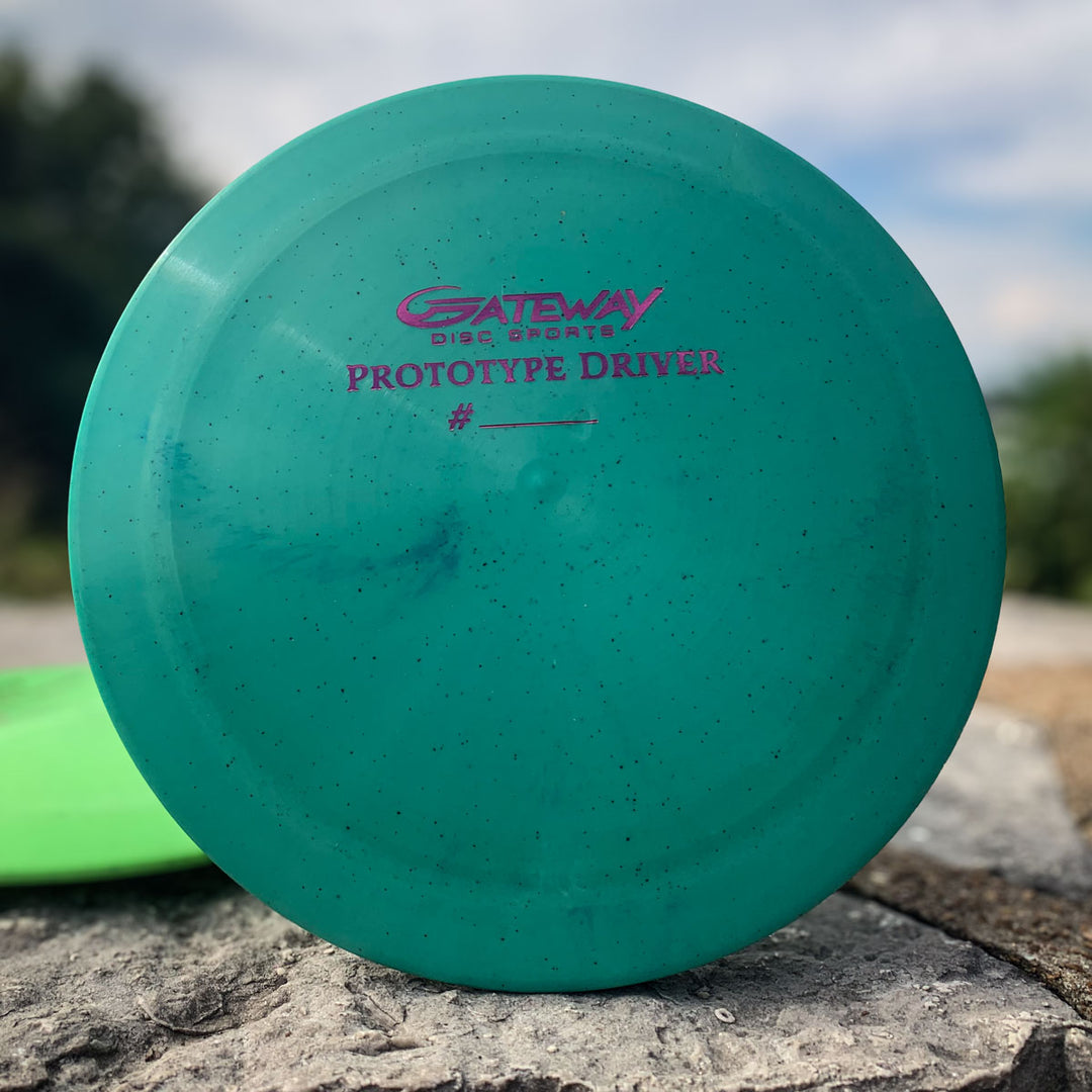 A teal Prototype 136 - NXT Hemp (Javelin) distance control driver, labeled "Gateway Prototype Driver" with a space for a number, rests on a stone surface outdoors.