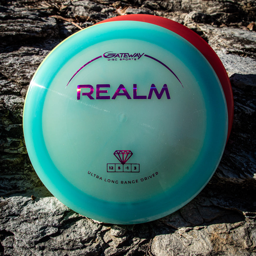 A teal and white Gateway Realm - Diamond distance driver, labeled "Ultra Long Range Driver," rests on a rocky surface in sunlight.