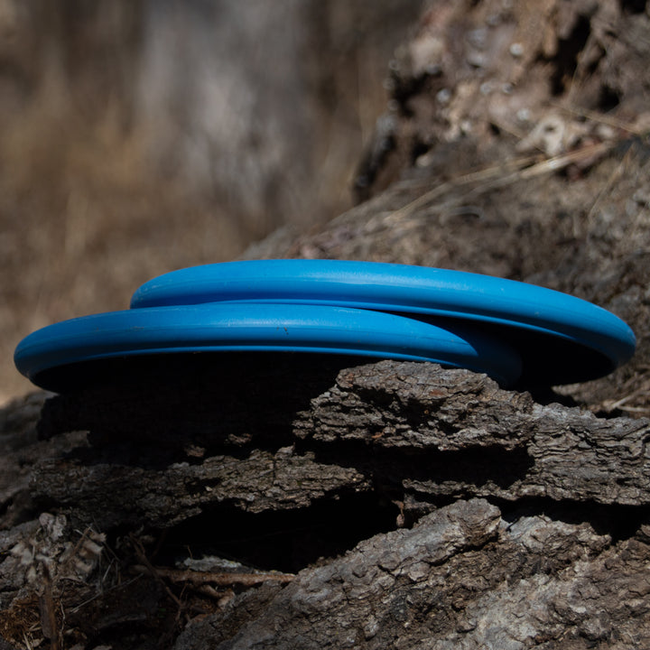 Two blue Retro Wizard - Eraser discs stacked on rough tree bark outdoors.