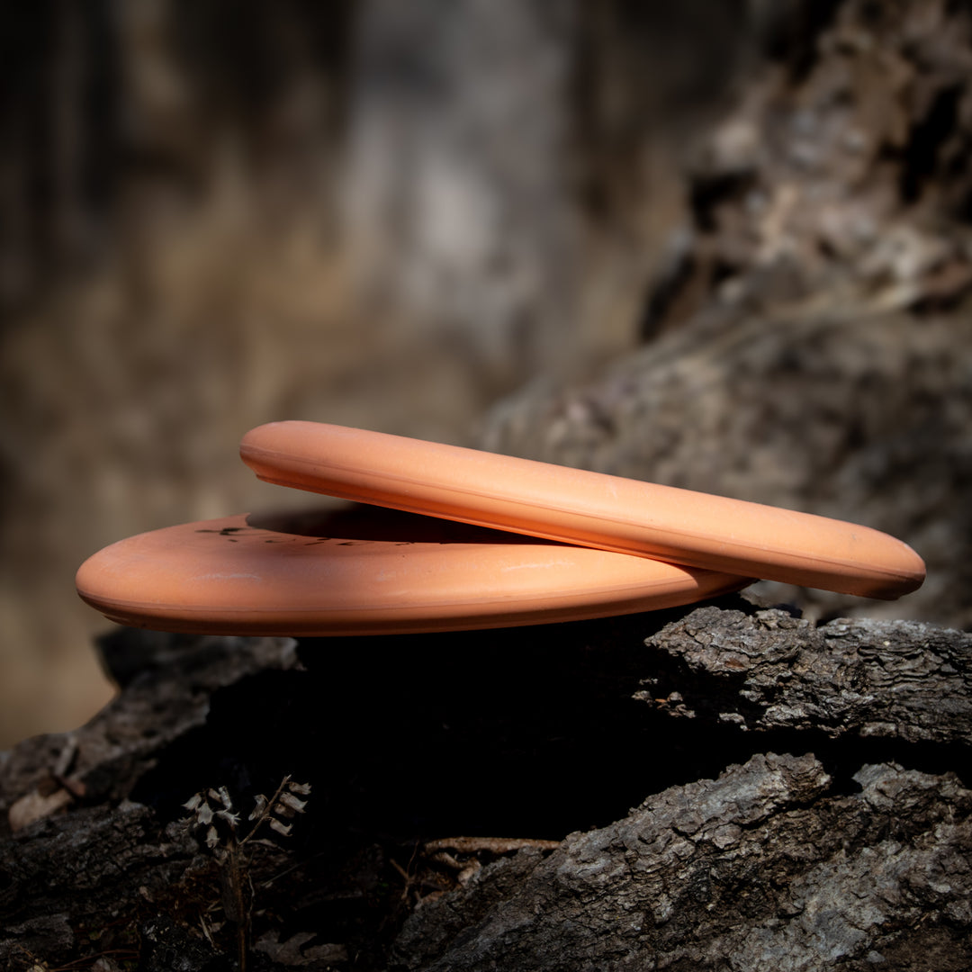 Two Retro Wizard - Eraser orange discs are stacked on a rough tree trunk, with a blurred natural background.