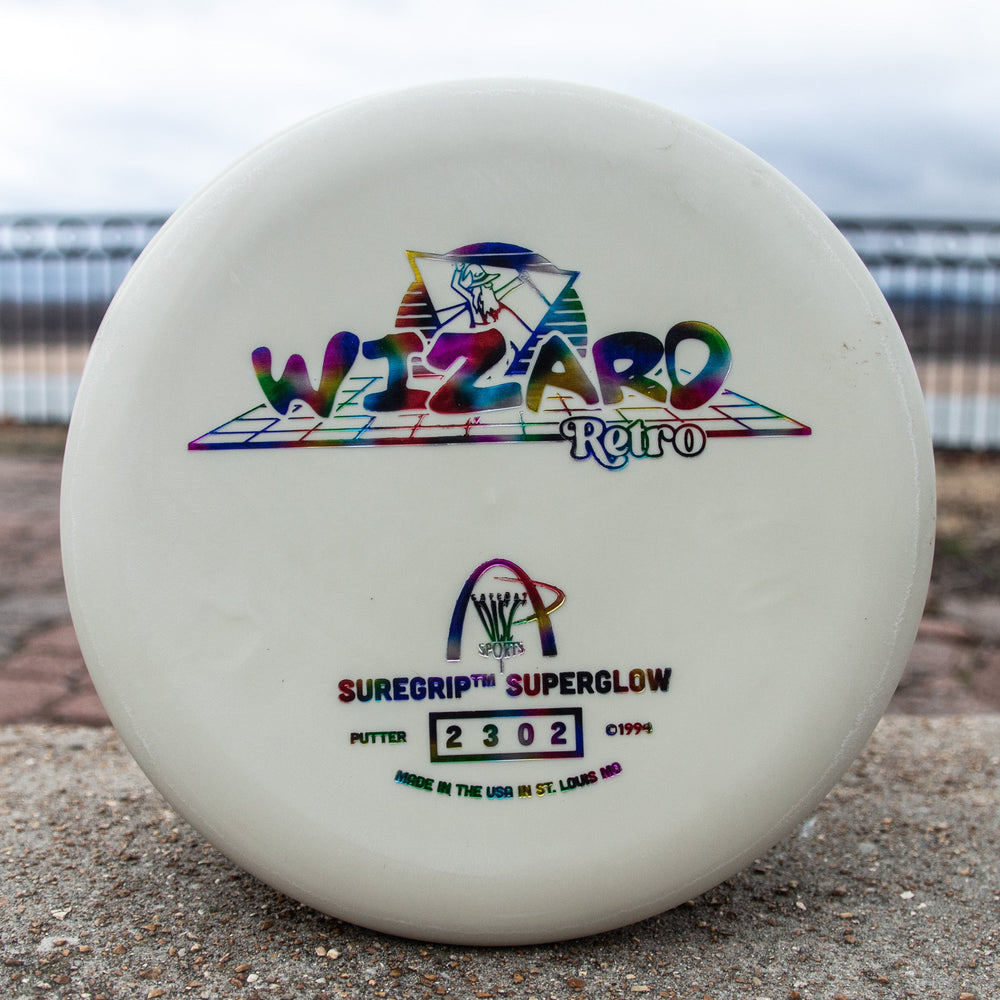 The Retro Wizard - SS Superglow is a white disc golf putter with colorful "Wizard Retro" text and logos, crafted with the Superglow formula for classic Gateway feel, plus "SureGrip SuperGlow" and serial number 2302 on the front.