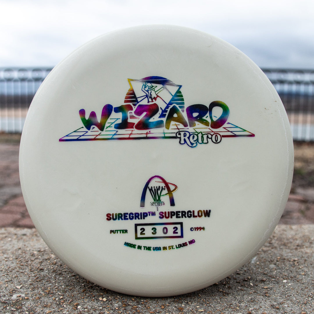 The Retro Wizard - SS Superglow is a white disc golf putter with colorful "Wizard Retro" text and logos, crafted with the Superglow formula for classic Gateway feel, plus "SureGrip SuperGlow" and serial number 2302 on the front.