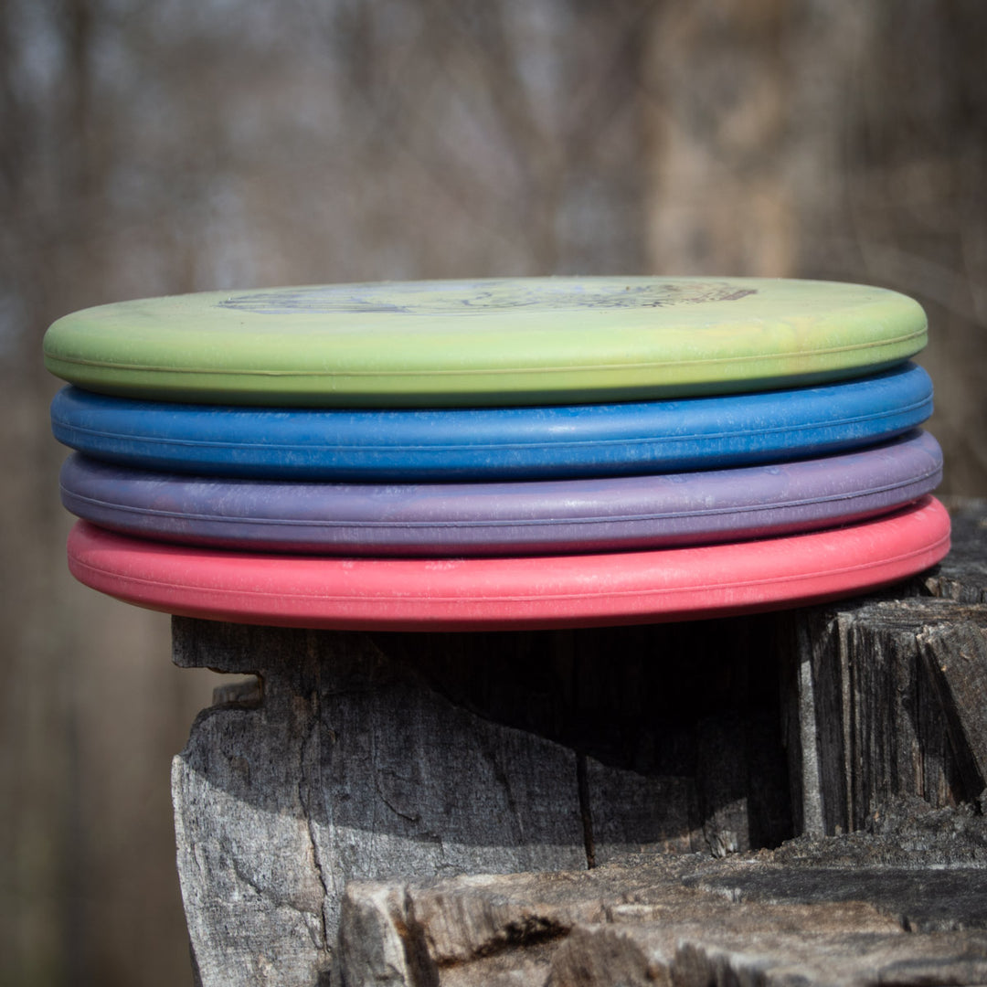 A stack of five Shaman - SSS - Mushroom discs with a Special Edition Stamp rests on a tree stump outdoors, with a blurred forest background.