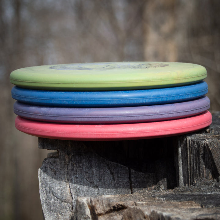 A stack of five Shaman - SSS - Mushroom discs with a Special Edition Stamp rests on a tree stump outdoors, with a blurred forest background.