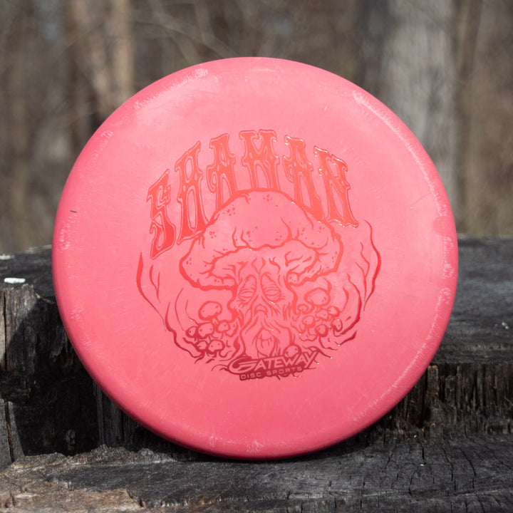 A red Shaman - SSS - Mushroom disc golf disc with a flat nose and Special Edition Stamp labeled "Gateway Disc Sports" rests on a tree stump outdoors.
