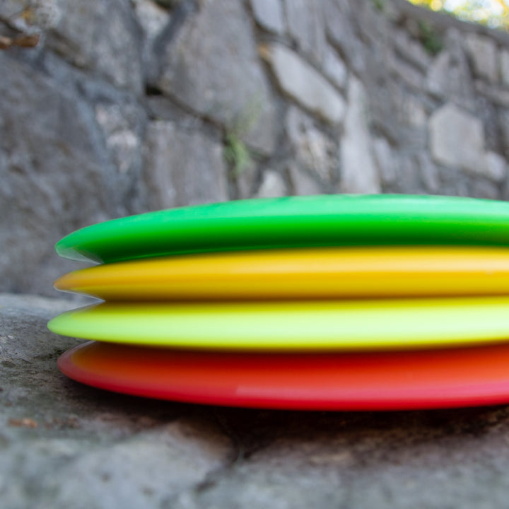 Four Spear - NXT discs, crafted from a durable plastic blend, are stacked on a stone surface with a stone wall in the background.
