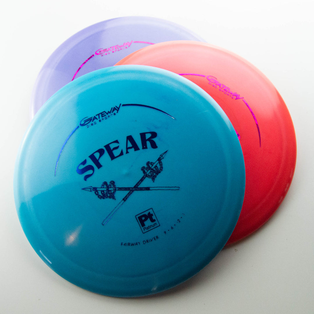 Three overlapping disc golf discs—blue, pink, and purple—labeled "Spear - Platinum" with a spear graphic on the blue disc. This 9 speed control driver ensures precise placement on every throw.