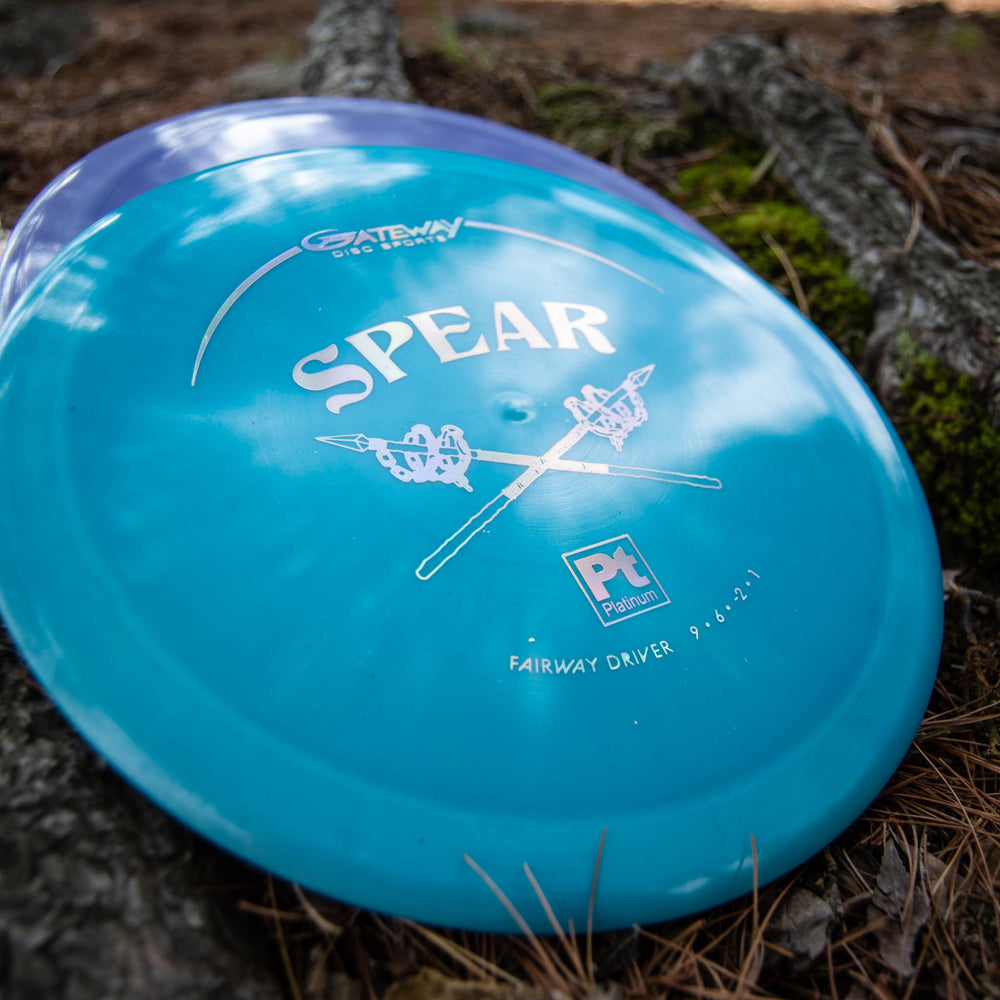 A teal Spear - Platinum 9 speed fairway driver rests among pine needles and tree roots, ideal for precise placement on your next round.