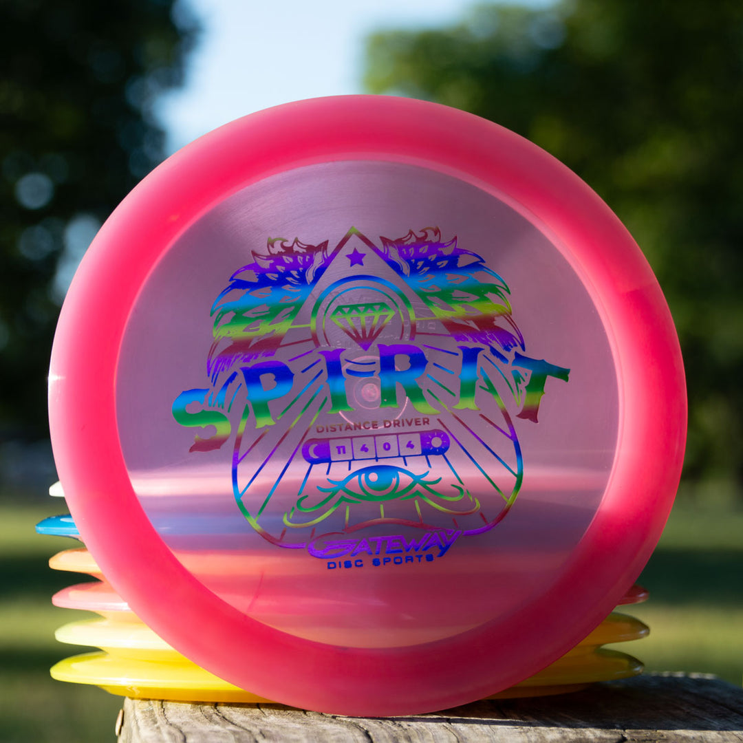A stack of colorful disc golf discs on a wooden surface outdoors, with the top disc labeled "Spirit - Diamond," a high speed overstable driver featuring a decorative lion graphic.