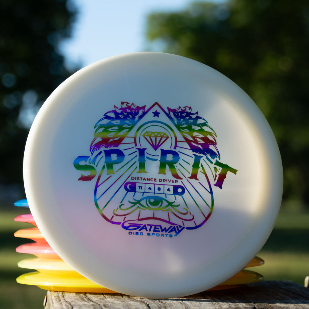 A white Spirit — Diamond long distance driver disc with a colorful geometric lion and "SPIRIT" logo sits atop a stack of other discs outdoors.