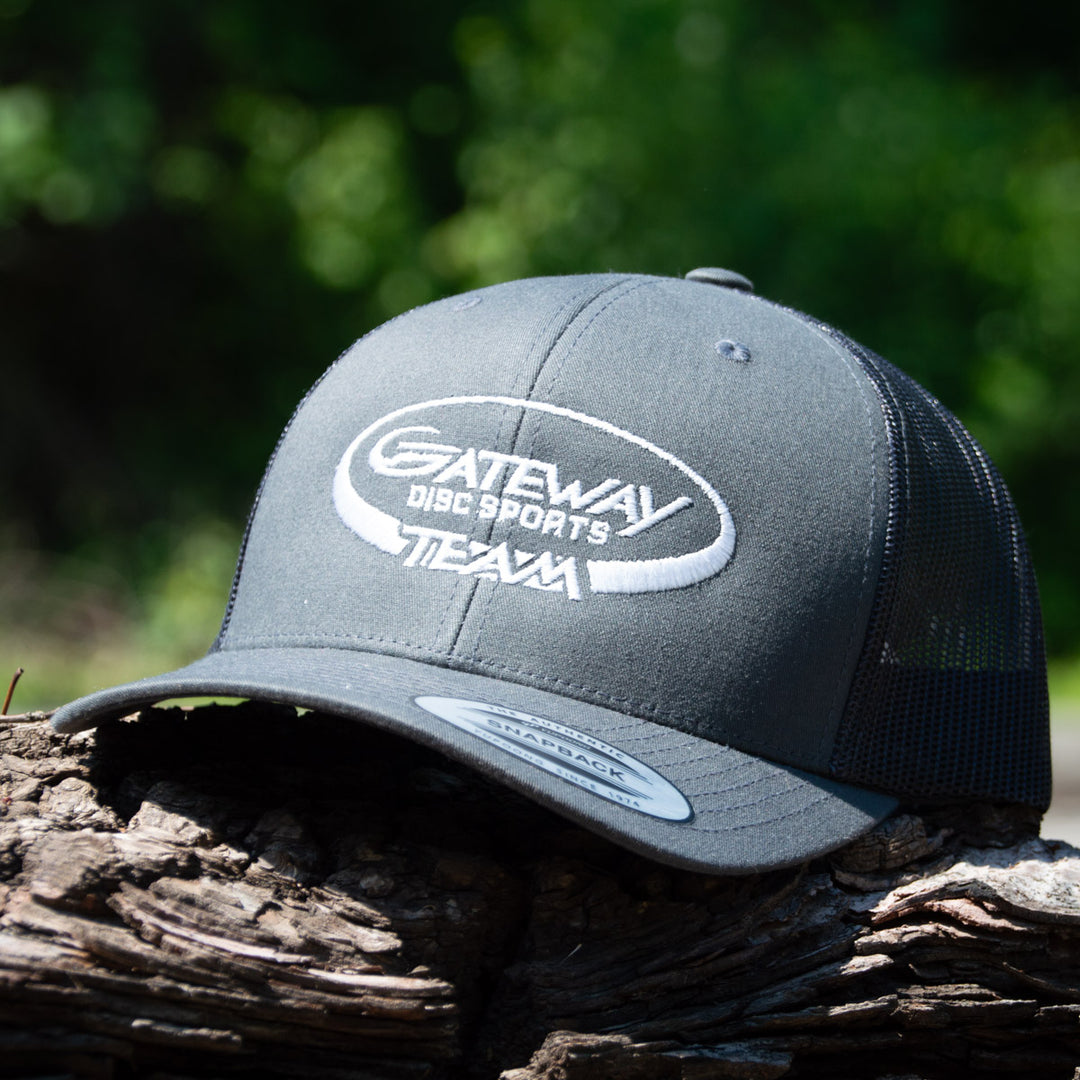 The Team Gateway Snap Back hat, a gray polyester-cotton cap with mesh back and "Gateway Disc Sports Team" embroidery, is shown resting on wood outdoors.