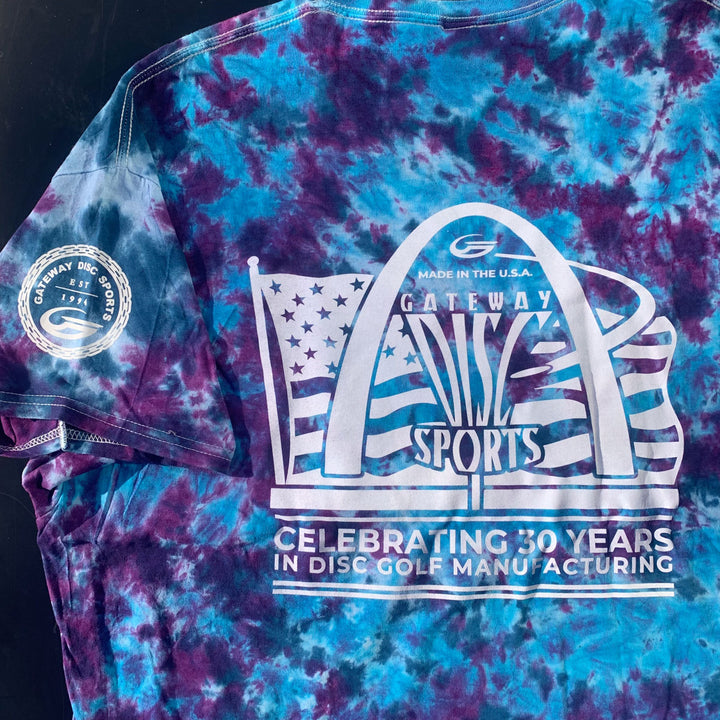 The 30th Anniversary Tie Dyed T-Shirt features Gateway Disc Sports' special logo—a stylized arch with flag—plus a sleeve patch and the text: "Celebrating 30 Years in Disc Golf Manufacturing." Made from hand-dyed cotton.