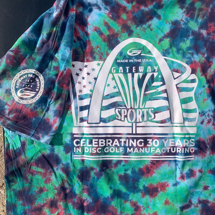 The 30th Anniversary Tie Dyed T-Shirt features a St. Louis Arch graphic, "Gateway Sports" anniversary logo, and "Celebrating 30 Years in Disc Golf Manufacturing" on the front, with a patch detail on the sleeve.
