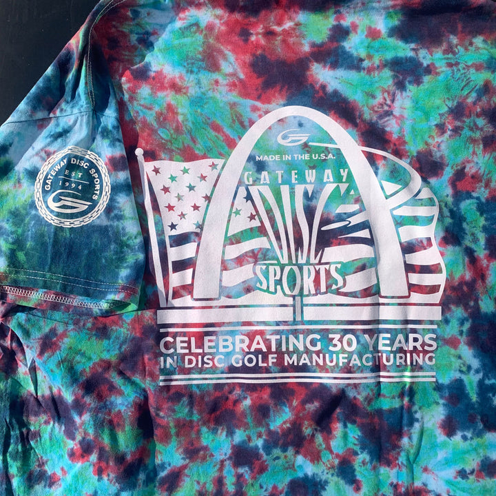 The 30th Anniversary - Tie Dyed T-Shirt is a hand-dyed cotton tee featuring the Gateway Disc Sports anniversary logo, arch graphic, and "Celebrating 30 years in disc golf manufacturing" text.