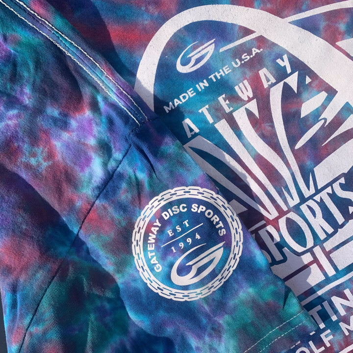 Close-up of a hand dyed, multicolored cotton "30th Anniversary - Tie Dyed T-Shirt" featuring white Gateway Disc Sports logos, an anniversary logo, and text such as "Made in the U.S.A." and "Est. 1994.