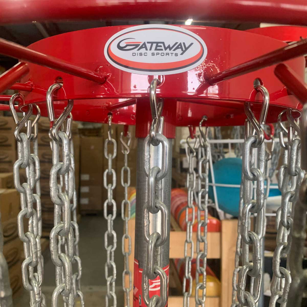 Close-up of the top section of a red Titan Pro 24 Portable Basket with hanging metal chains, showcased as a championship-level portable disc golf target by Gateway Disc Sports in an indoor storage area.