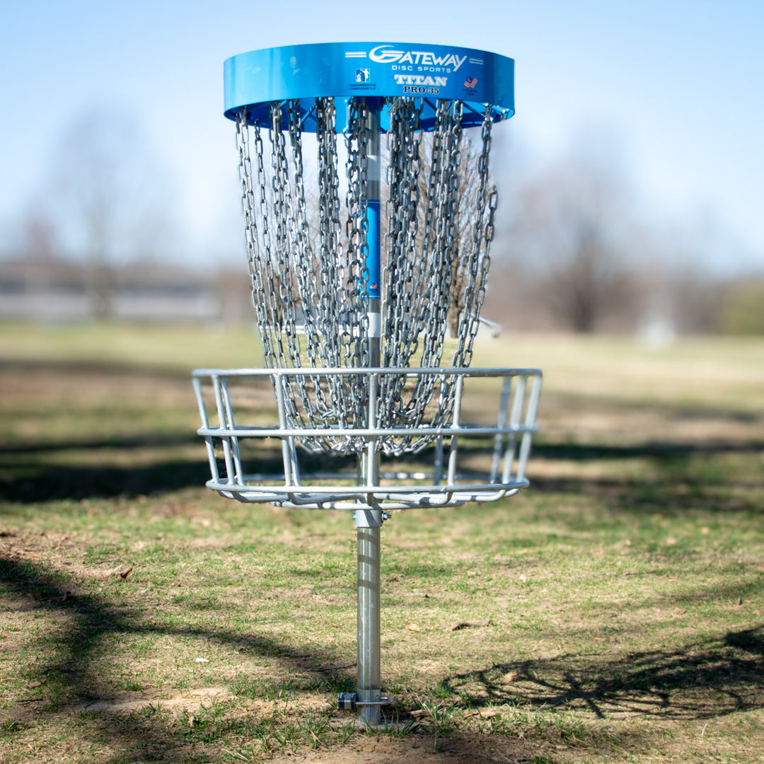 A set of 9 Titan Pro 35 permanent disc golf baskets with sturdy chains stands on a grassy field under a clear sky.