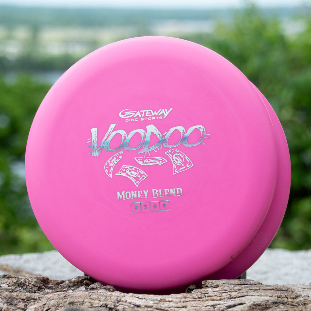 Two pink Voodoo - Money disc golf putters, known for their stability and reliability, are shown outdoors on a stone surface with greenery in the background.
