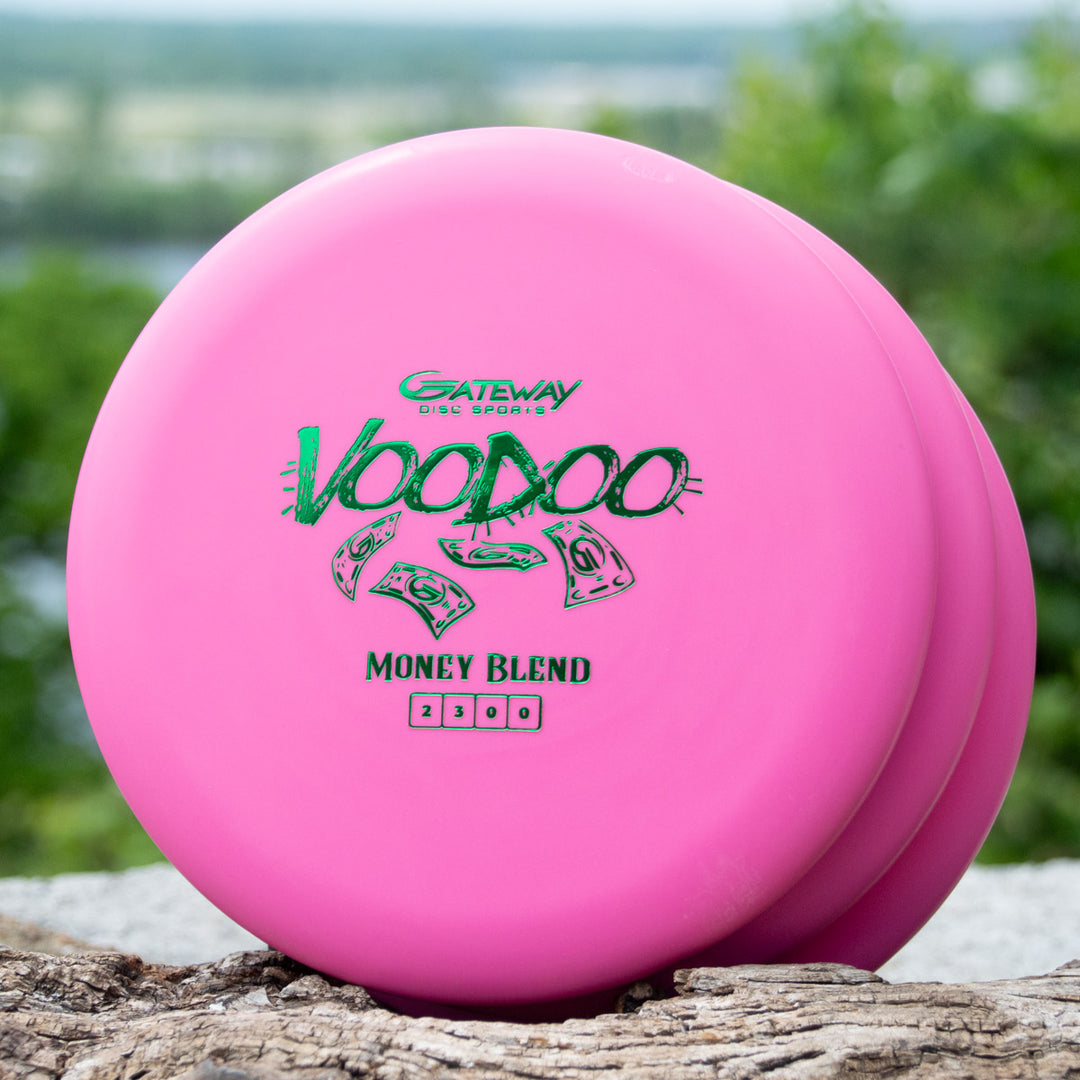 Three pink Gateway Voodoo - Money discs, renowned as stable workhorse putters, rest on a wooden surface with greenery in the background.