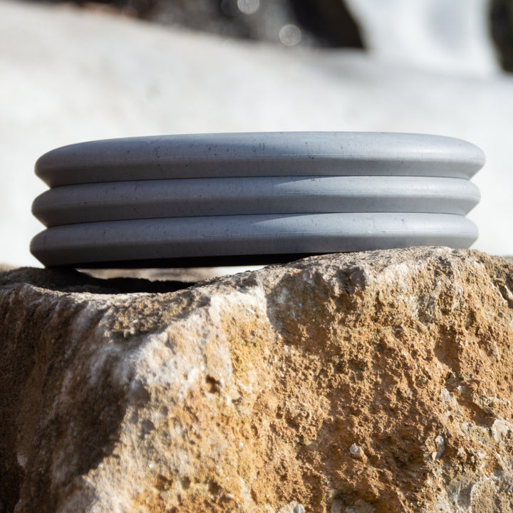 A round, gray Warlock - Lunar with ridges rests on a rough, light brown stone surface outdoors, evoking the mystery of an enchanted artifact.