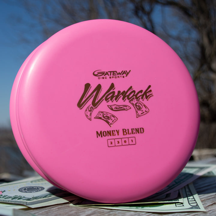 A pink Warlock - Money disc from the 2301 run is placed outdoors on top of several U.S. dollar bills.