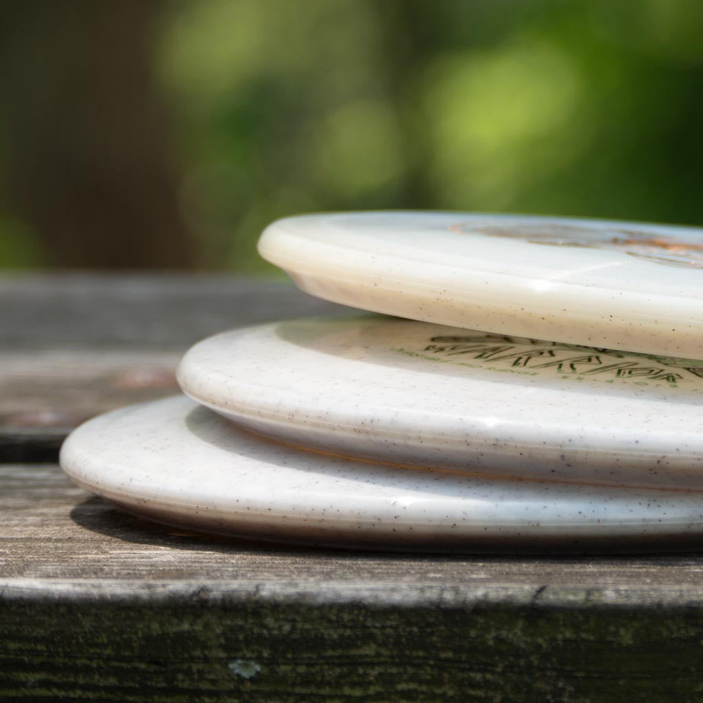 Three Warrior - Diamond Hemp discs stacked outdoors on a wooden surface with a blurred green background—ideal for players seeking reliable glide on the course.