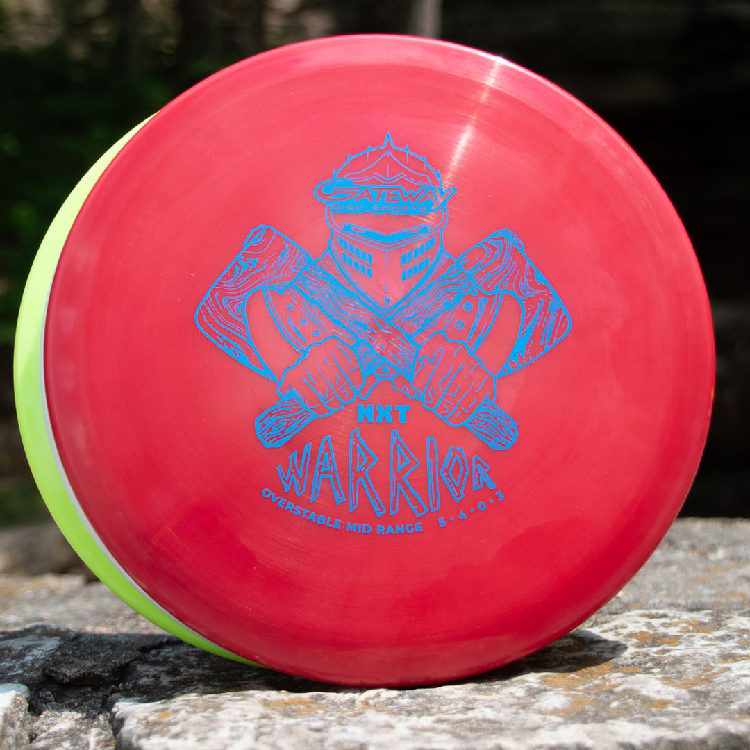 The Warrior - NXT is a red overstable mid-range disc with a blue graphic of a helmeted figure wielding two clubs. Flight numbers: 5/4/0/3.