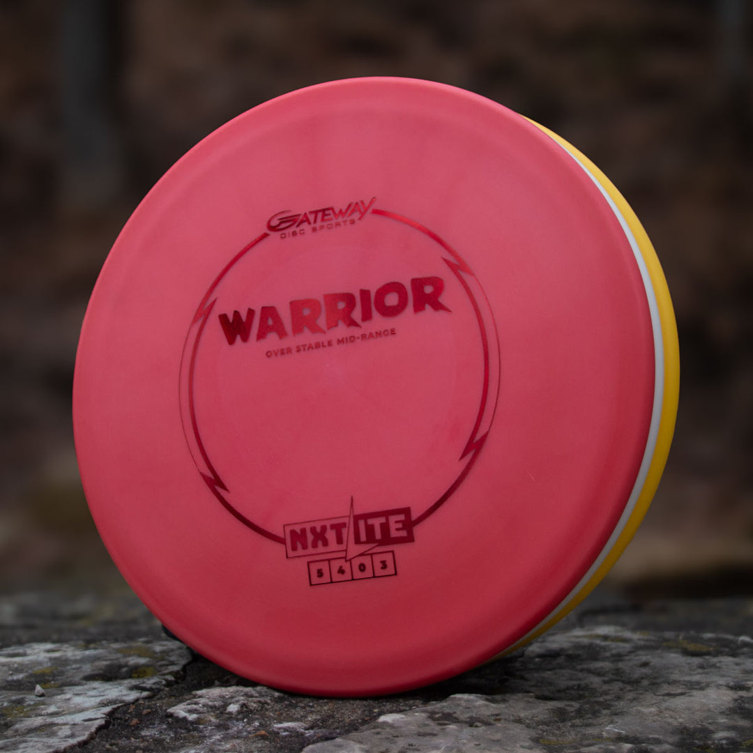 A Gateway Disc Sports Warrior - NXT Lite mid-range disc in red rests on stone—perfect for controlled hyzer approaches.