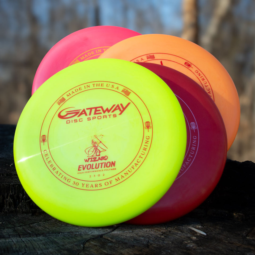 Three vibrant Gateway Wizard - Evolution - Neon discs in yellow, orange, and red stacked on a tree stump outdoors with blurred trees in the background.