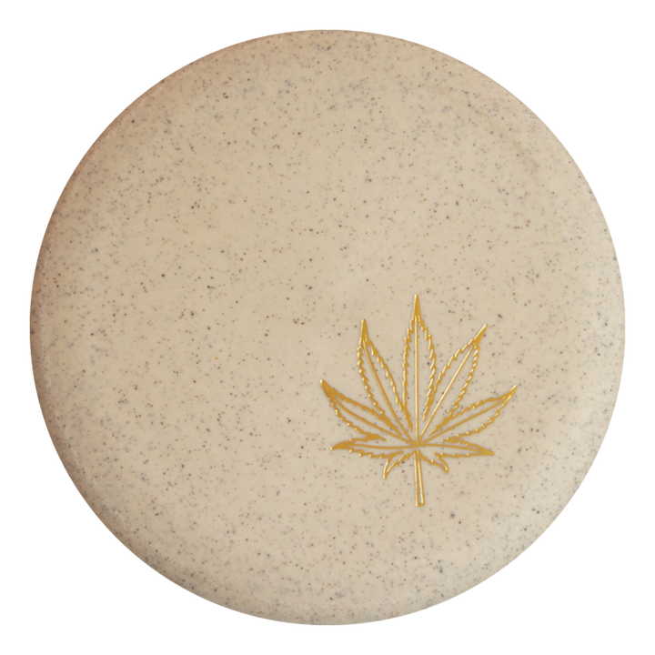 Round beige soap bar with small speckles and a gold cannabis leaf design, echoing the signature look of Wizard Leaf Suregrip Putters by Gateway Disc Sports.
