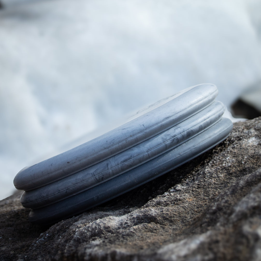 The Wizard - Lunar, a silver disc-shaped putt & approach disc with ridged edges resembling the original Wizard, rests on a rough gray rock surface outdoors.
